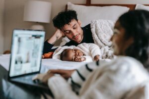 happy young father admiring sleeping baby near ethnic wife using netbook