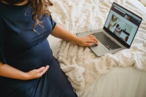 crop pregnant woman watching photos on laptop screen at home